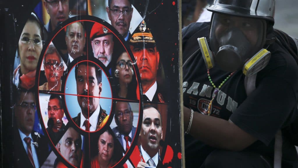 | An anti government protester holds a homemade shield brandished with photos of President Nicolas Maduro government officials and a gun sight during clashes with security forces blocking a march to the Supreme Court in Caracas Venezuela Saturday July 22 2017 Protesters rallied Saturday in the Venezuelan capital for a march toward the embattled nation | MR Online's Supreme Court, opposing Maduro's plan to rewrite the constitution. (AP Photo/Fernando Llano)