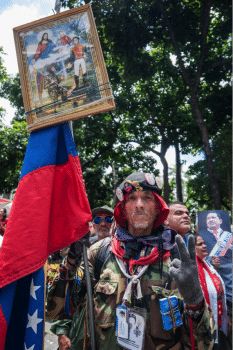 | A man gathers around Bolívar Square with Simón Bolívar and Chávez portraits and a copy of 99s Venezuelan Constitution | MR Online