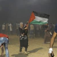 A Palestinian woman waves the national flag on Nakba day, a day after Israeli troops massacred 60 unarmed civilians