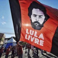 In this July 8, 2018 file photo, a supporter of former Brazilian President Luiz Inacio Lula da Silva waves a banner decorated with an image depicting da Silva and message that reads in Portuguese: "Free Lula," in front of the Federal Police Department where he is serving jail time, in Curitiba, Brazil. | Photo Credit: AP