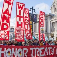 People protesting the Dakota Access Pipeline march past San Francisco City Hall in 2016.  Photo by Pax Ahimsa Gethen [CC BY-SA 4.0 (https-::creativecommons.org:licenses:by-sa:4.0)].