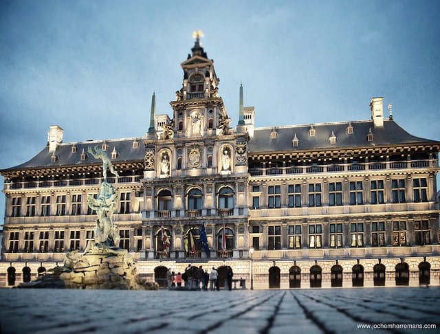 | The City Hall Dutch Stadhuis of Antwerp Belgium stands on the western side of Antwerps Grote Markt Great Market Square Erected between 1561 and 1565 after designs made by Cornelis Floris de Vriendt and several other architects and artists this Renaissance building incorporates both Flemish and Italian influences The City Hall is inscribed on UNESCOs World Heritage List along with the belfries of Belgium and France Margaret of Parma hands over the keys to the city by Henri Leys In the 16th century Antwerp became one of the busiest trading ports and most prosperous cities in Northern Europe The municipal authorities wished to replace Antwerps small medieval town hall with a more imposing structure befitting the prosperity of the great port city Antwerp architect Domien de Waghemakere drafted a plan c 1540 for a new building in a style typical of the monumental Gothic town halls of Flanders and Brabant But the threat of war prevented any progress on the project The building materiasl intended for the city hall were instead used to shore up the city defenses Not until about 1560 new plans were developed In the meantime Gothic architecture had gone out of fashion The new designs for the city hall were in the new Renaissance style Completed in 1565 the building lasted hardly a decade before being burnt to a shell in the Spanish Fury of 1576 It was restored three years later The low arcaded ground story is of rusticated stone and at one time housed little shops Above are two stories with Doric and Ionic columns separating large mullioned windows and a fourth story forming an open gallery The richly ornamented central section which rises above the eaves in diminishing stages holds female statues representing Justice Prudence and the Virgin Mary and bears the coats of arms of the Duchy of Brabant the Spanish Habsburgs and the Margraviate of Antwerp Renovations during the late 19th century by architects Pierre Bruno Bourla Joseph | MR Online
