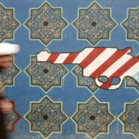 An Iranian cleric walks past mural on the wall of the former U.S. embassy in Tehran