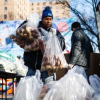 A volunteer wearing protective gloves organizes pre-bagged food donations at a City Harvest's Bed-Stuy Mobile Market operating in the Tomkins Houses area, Wednesday, March 18, 2020, in New York. Mayor Bill de Blasio said New York City residents should be prepared for the possibility of a "shelter in place" order within days. De Blasio said Tuesday no decision had been made yet, but he wants city and state officials to make a decision within 48 hours given given the fast spread of the coronavirus. (AP Photo/John Minchillo)
