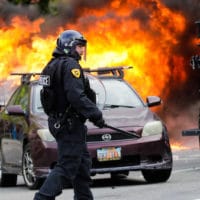 A policeman walks in front of a burning vehicle as protesters demonstrate, May 30, 2020, in Salt Lake City. Rick Bowmer | AP