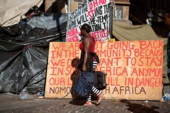 | A woman walks with her belongings past a sign as hundreds of people from various African countries are evicted from the makeshift camp they are occupying around the Central Methodist Mission in Cape Town 1 March 2020 Photo Rodger Bosch AFP Getty Images | MR Online