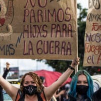 In Bogotá during Colombia’s national strike, two women hold placards that say, “We didn’t give birth to children of war” and “They got firearms, we got fire in our soul” / credit: Antonio Cascio