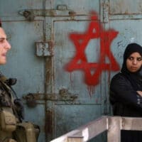 AN ISRAELI SOLDIER KEEPS GUARD NEAR A PALESTINIAN WOMAN STANDING NEXT TO STAR OF DAVID GRAFFITI SPRAYED BY ISRAELI SETTLERS AT AN ARMY CHECKPOINT IN THE CENTER OF HEBRON, MAY 18, 2009. (PHOTO: MENAHEM KAHANA/AFP/GETTY IMAGES)