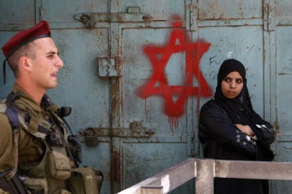 | AN ISRAELI SOLDIER KEEPS GUARD NEAR A PALESTINIAN WOMAN STANDING NEXT TO STAR OF DAVID GRAFFITI SPRAYED BY ISRAELI SETTLERS AT AN ARMY CHECKPOINT IN THE CENTER OF HEBRON MAY 18 2009 PHOTO MENAHEM KAHANAAFPGETTY IMAGES | MR Online