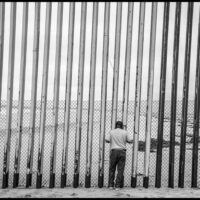 A man on the Mexican side of the border wall between Mexico and the U.S. looks through the bars, where the wall runs into the Pacific Ocean