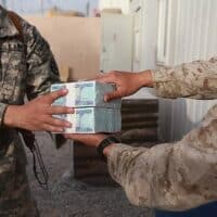 U.S. Marine Corps Cpl. David Che, right, a supply warehouse clerk with Headquarters and Service Company, 1st Marine Logistics Group (Forward), hands Afghan currency to Army 1st Lt. Manuel Jimenez April 7, 2014
