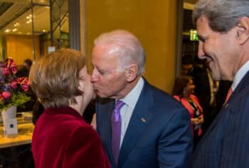 | Merkel and Joe Biden kissing at 2015 Munich Security Conference with then Secretary of State John Kerry MuellerMSCFlickr | MR Online