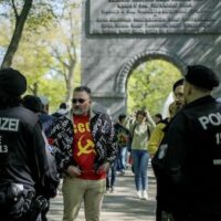 Police officers ask a man wearing a shirt showing hammer and sickle to close his jacket outside the tomb of the Soviet War memorial at the park in Treptow, during the 78th anniversary of Victory Day and the end of WWII in Europe, in Berlin, Germany, Tuesday, May 9, 2023. [AP Photo/Markus Schreiber]