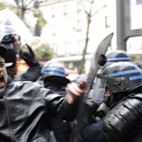 Riot police officers charge a man holding his phone during a protest rally in Paris, France, Saturday, Dec.12, 2020.